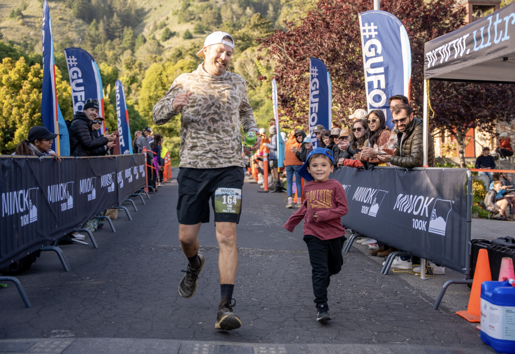 A tall man and his young son cross the finish line together. 